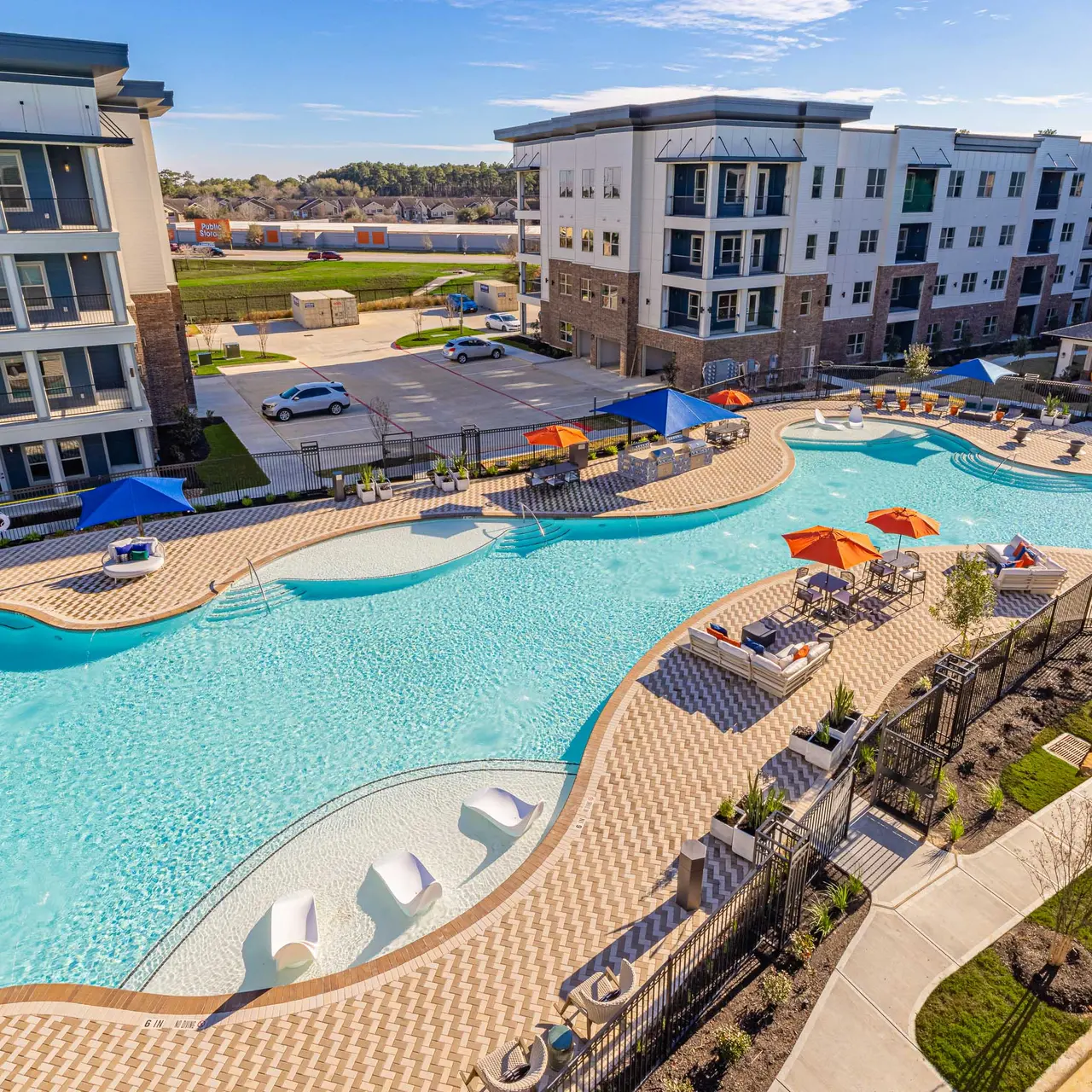 A wide view of a luxurious residential pool area featuring a winding pool with various seating areas and colorful umbrellas.