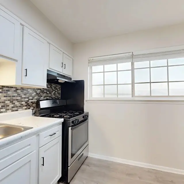 Modern kitchen featuring white cabinets, a tiled backsplash, and stainless steel appliances including a stove and refrigerator.