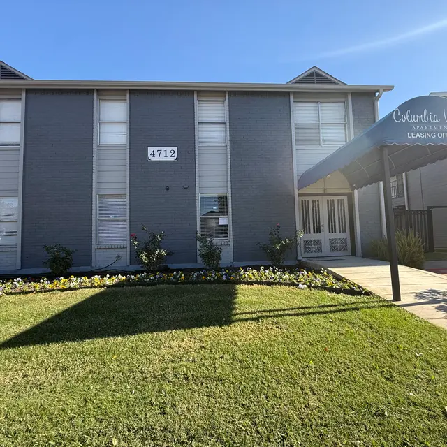 Exterior view of the Columbia Villas Learning Office building, featuring a gray facade, a walkway, and a green lawn with flowers.