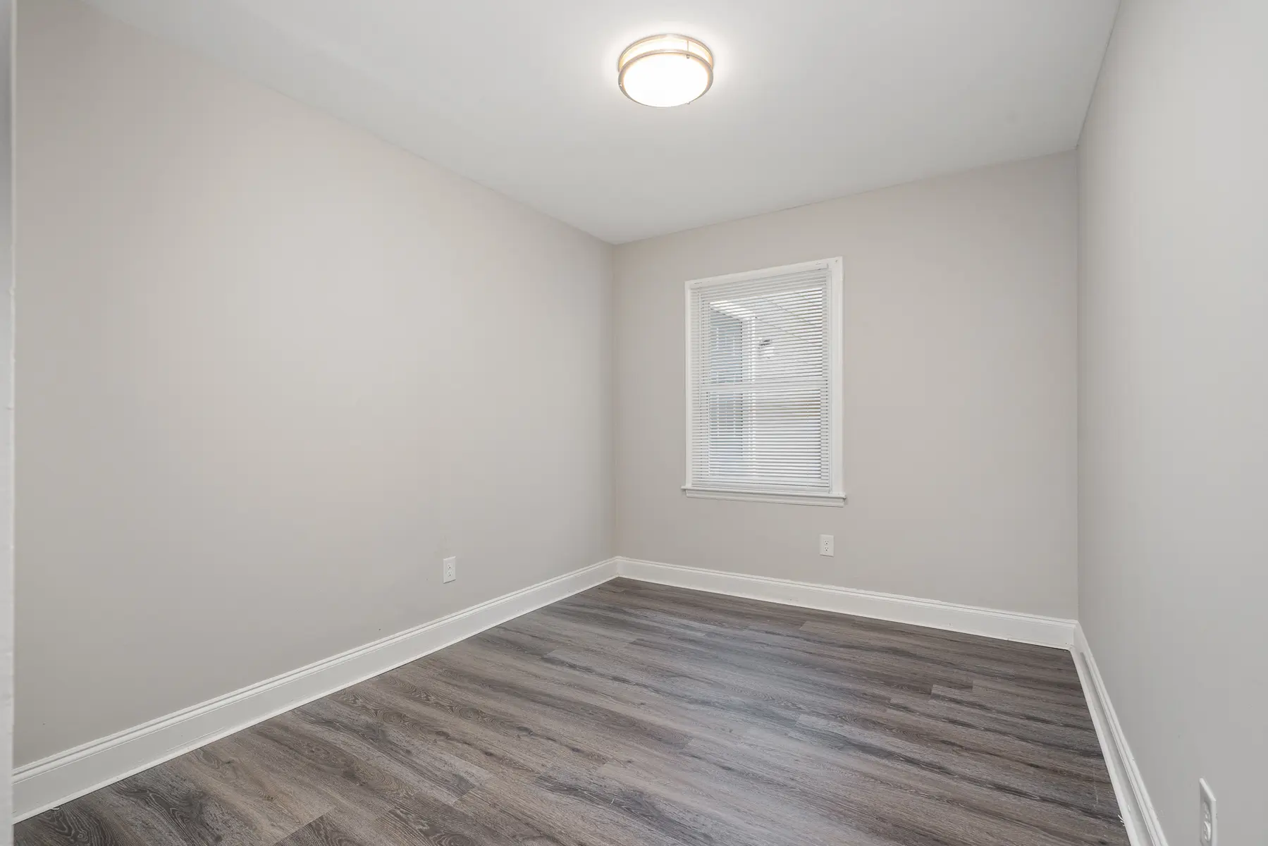 An empty, minimalistic bedroom with light gray walls and a window letting in daylight.