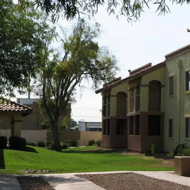 Residential Apartment Complex A view of a residential apartment complex with green lawns and trees. Two buildings are visible with balconies and a pathway leading through the area.