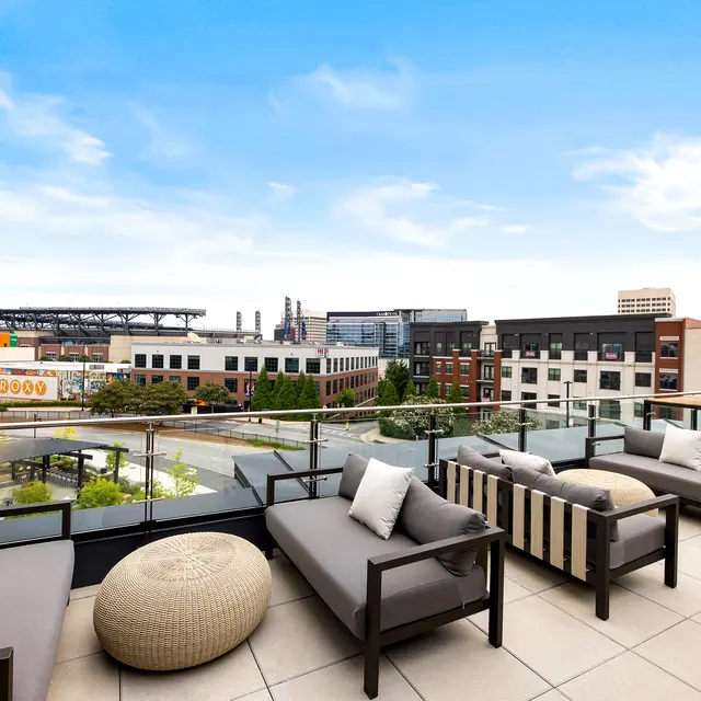 A stylish balcony with modern furniture overlooking a vibrant urban area, featuring a skyline with a blue sky.