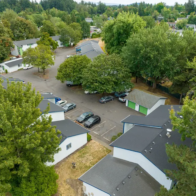 Aerial View of Residential Complex Aerial view of a residential condominium complex surrounded by trees, with parked cars visible and a winding driveway.
