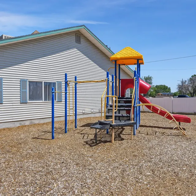 Playground Area with Climbing Structures A colorful playground with slides and climbing structures in a gravel area beside a building.