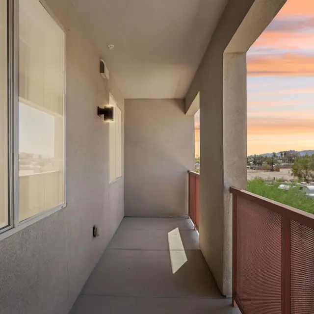 Sunset View from Modern Balcony A modern balcony with a railing overlooking a scenic sunset view. The balcony features gray walls and floors with large windows letting in natural light.