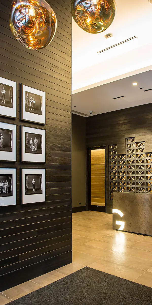 The Gallery on Wells - Modern lobby with dark wood walls, framed black-and-white photos, a sleek reception desk, and decorative lighting fixtures.
