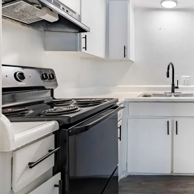 A modern kitchen featuring a black stove, white cabinets, and a stainless steel sink.