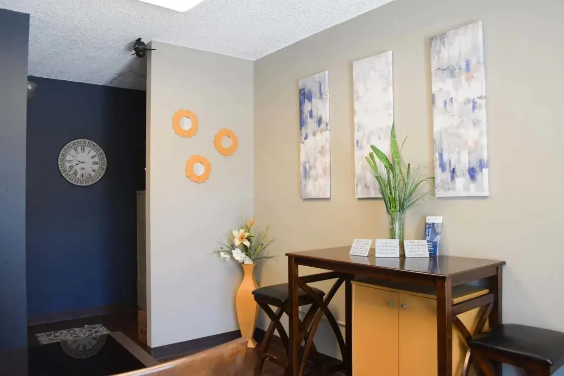 Modern Interior Entryway A cozy interior space featuring a small wooden table with stools, decorative wall panels, a flower vase, and a clock on the wall.