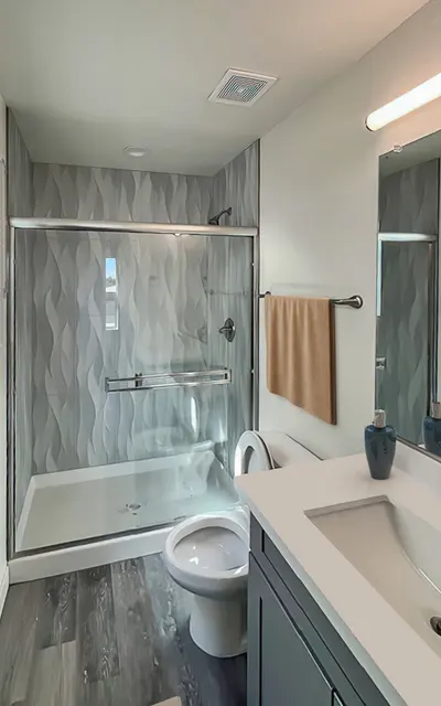 Raymond Place Dog-Friendly Townhouses in South Phoenix AZ - Raymond Place - Bright Bathroom with Wood Flooring, Glass Shower with Grey Walls, Vanity with Grey Cabinetry and White-Topped Sink, Mirror, and Towel Rack