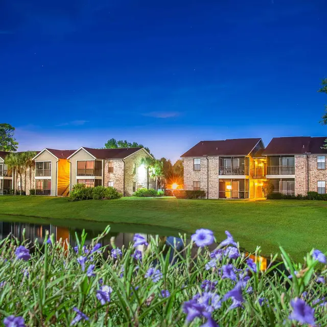 Nighttime view of Venice, FL apartments with balconies, a lakefront setting, and plants.