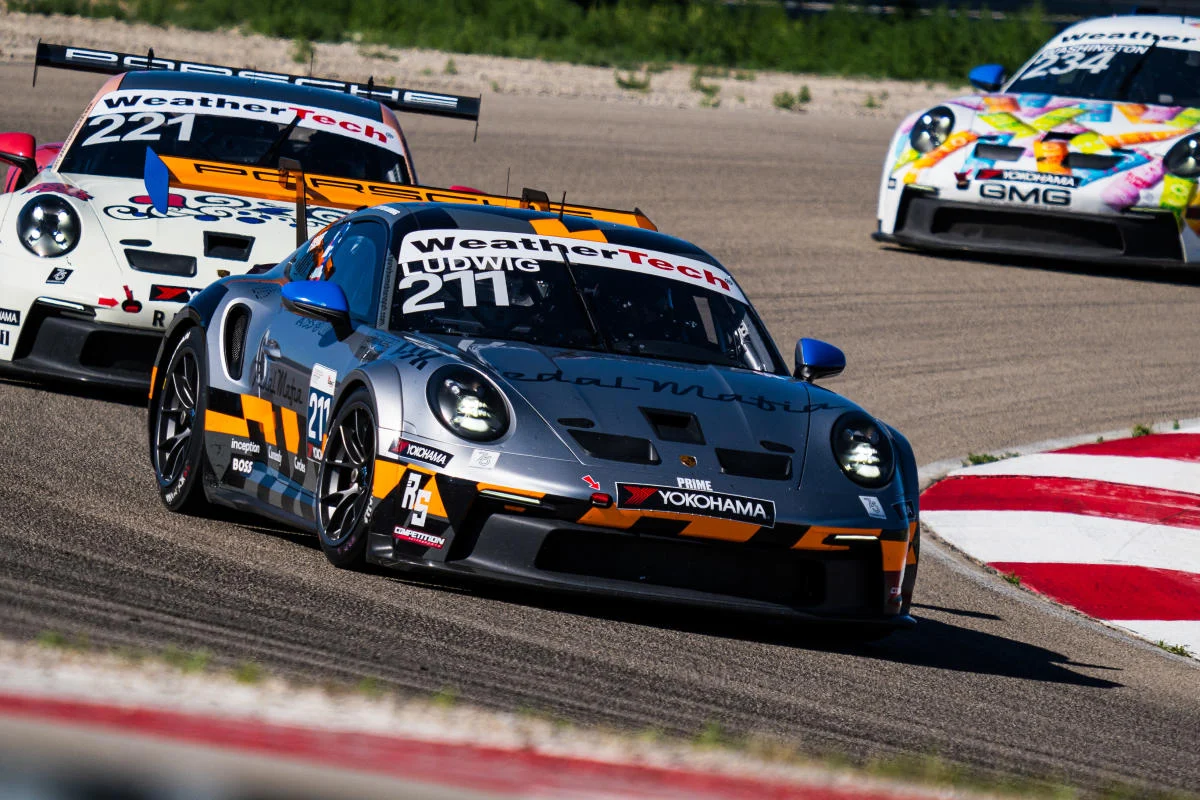 Porsche Racing Action Three racing cars competing on a track, with a focus on the blue and gray Porsche with the number 211 in front.