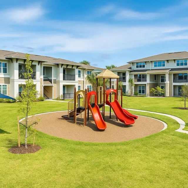 Playground in Residential Community A vibrant playground with two red slides surrounded by green grass and newly planted trees, with residential buildings in the background.