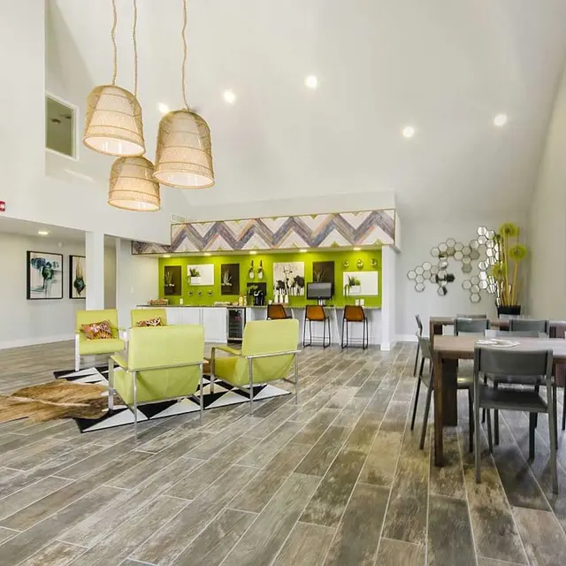The Edge Apartments Spacious resident clubhouse with hardwood flooring, coffee bar, seating area, and two tables with chairs by large windows.