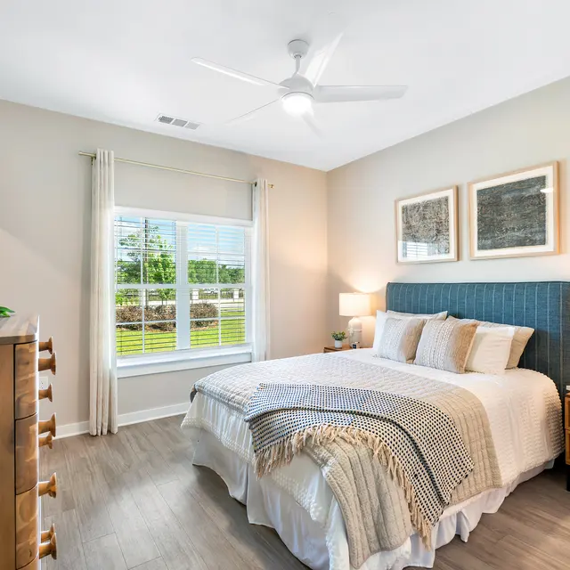 Modern Bedroom Interior A modern bedroom featuring a large bed with decorative pillows, a blue headboard, nightstands with lamps, and a window allowing natural light. The walls are light-colored, and there is a wooden dresser against one wall.