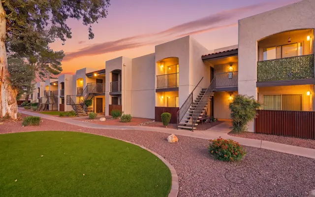 A picturesque view of an apartment complex during sunset, featuring lighted balconies and well-maintained landscaping.