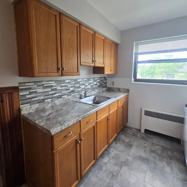 Modern Kitchen Design A modern kitchen with wooden cabinetry, a granite countertop, and a stainless steel sink beneath a window.