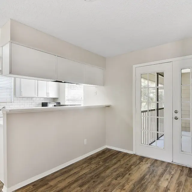 Living area next to a kitchen, with hardwood-style flooring facing french doors leading to a balcony.