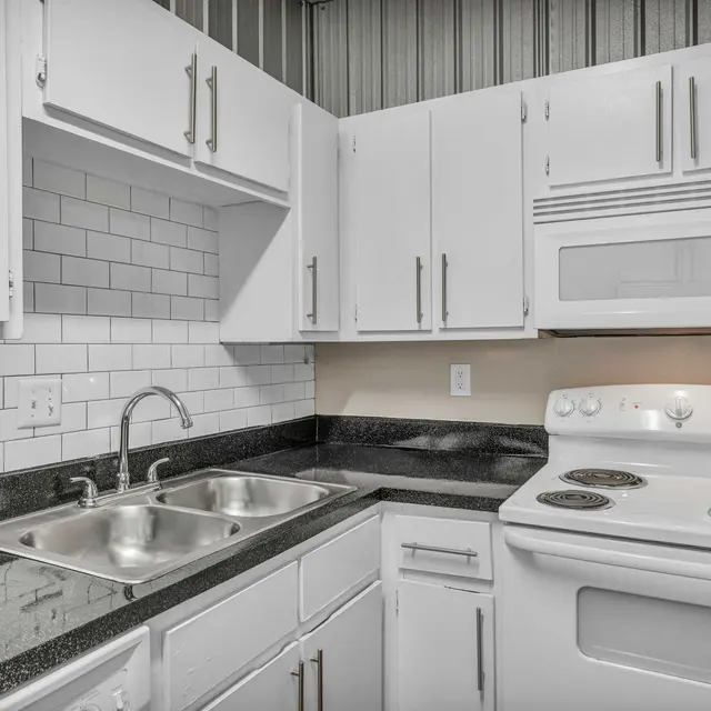 A kitchen with white cabinets, white appliances, white subway tile backsplash, granite countertops, and a double basin sink.