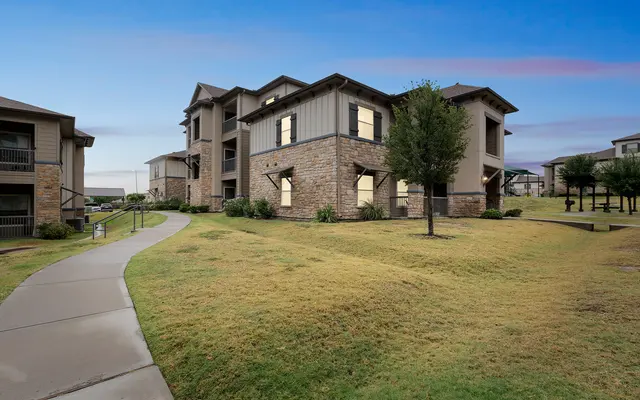 Modern Apartment Complex at Twilight A modern apartment complex with stone and stucco facades, surrounded by green grass and neatly trimmed bushes, under a twilight sky.