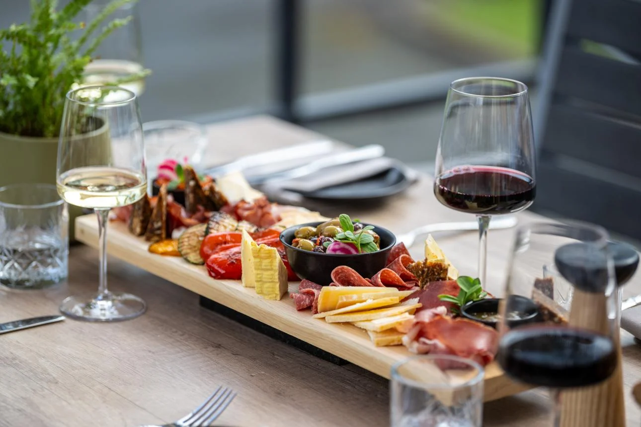 Gourmet Charcuterie Experience A wooden platter filled with various cheeses, meats, olives, and garnishes, accompanied by glasses of red and white wine on a dining table.