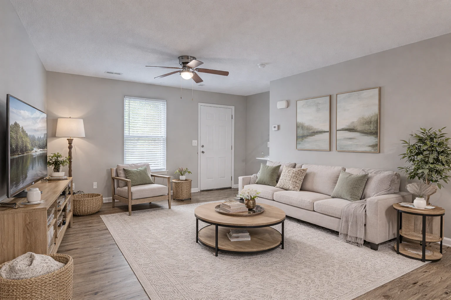 A modern living room with a beige sofa, wooden coffee table, potted plants, and wall art. There's a TV on the left and a window with blinds.