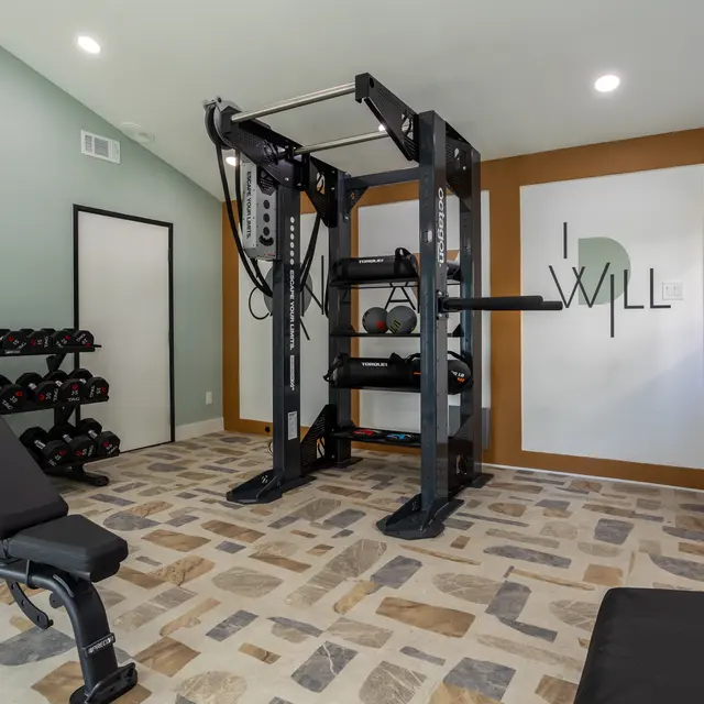 Interior of a modern gym featuring a weight bench, strength training machine, dumbbell rack, and motivational wall art.