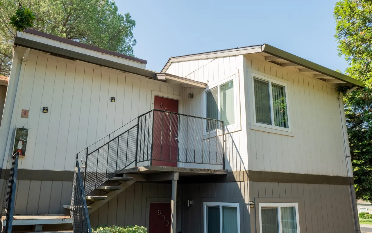 Exterior view of a two-story apartment building with a staircase leading up to a red door.