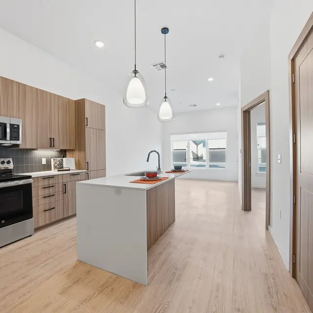 Modern kitchen with wooden cabinets, stainless steel appliances, a central island, and large windows allowing natural light.