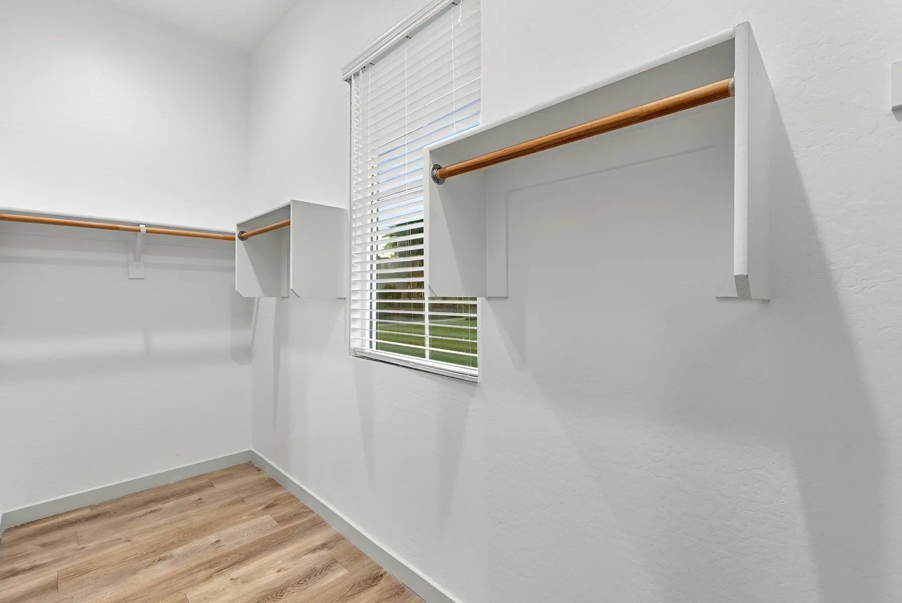 A spacious closet with white walls, two wooden rods for hanging clothes, and a window letting in natural light.