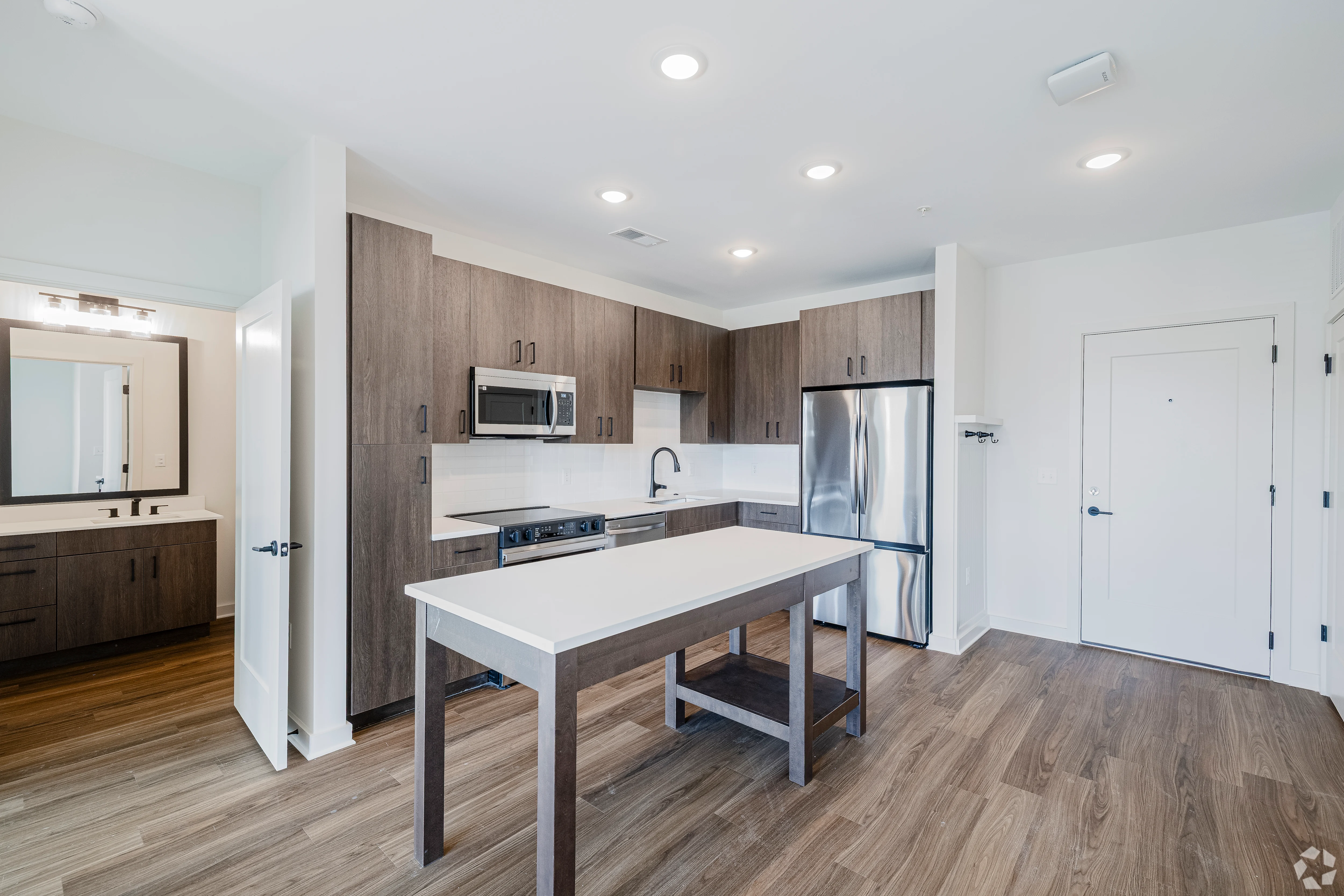 A modern kitchen with wooden cabinets and a central island. Stainless steel appliances are visible, along with a double sink. The kitchen features an open layout with good natural lighting.
