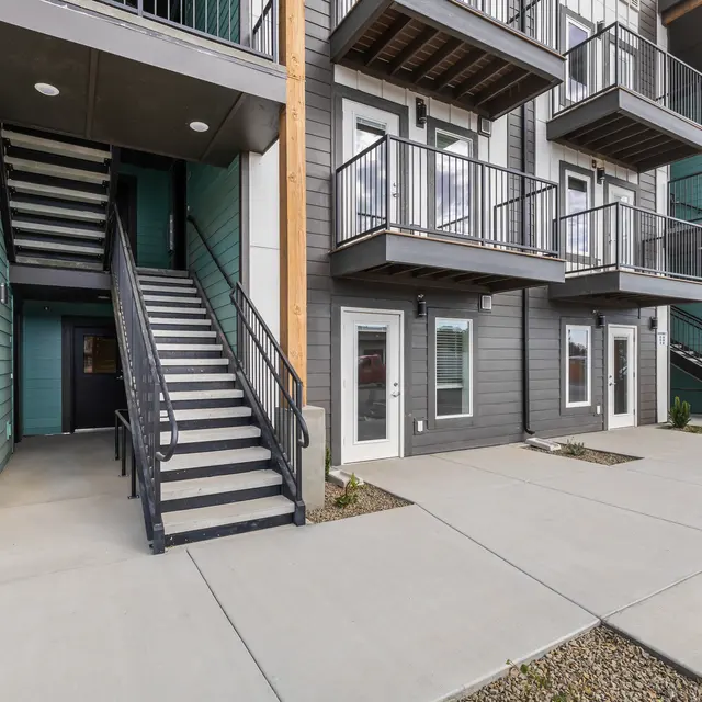 Exterior view of a modern apartment complex featuring a multi-level building with balconies and a staircase.