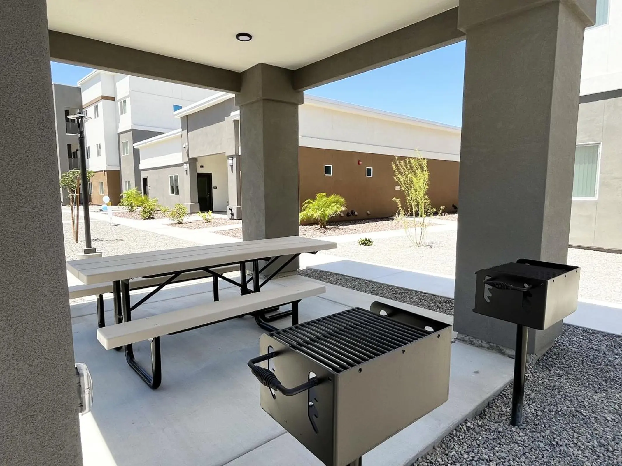 Picnic table and grill beneath a shaded outdoor structure.