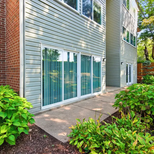 Exterior view of a modern apartment building with large glass sliding doors and greenery in the foreground.