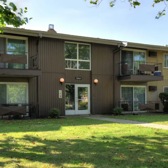 Exterior view of a two-story apartment building featuring a brown facade, balconies, and a lawn area in front.