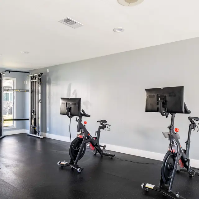 A modern gym interior featuring two exercise bikes with screens and a cable machine in the background.
