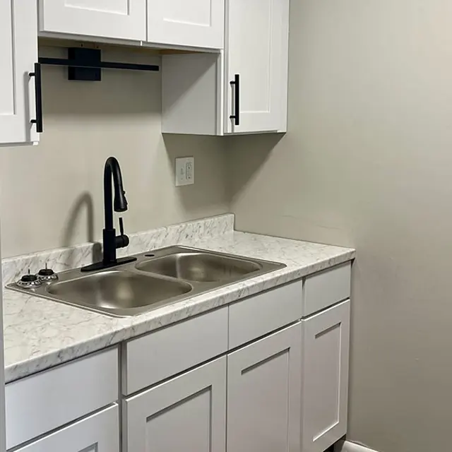 A modern kitchen sink area with white cabinets and a marble countertop, featuring a faucet and dual sinks.