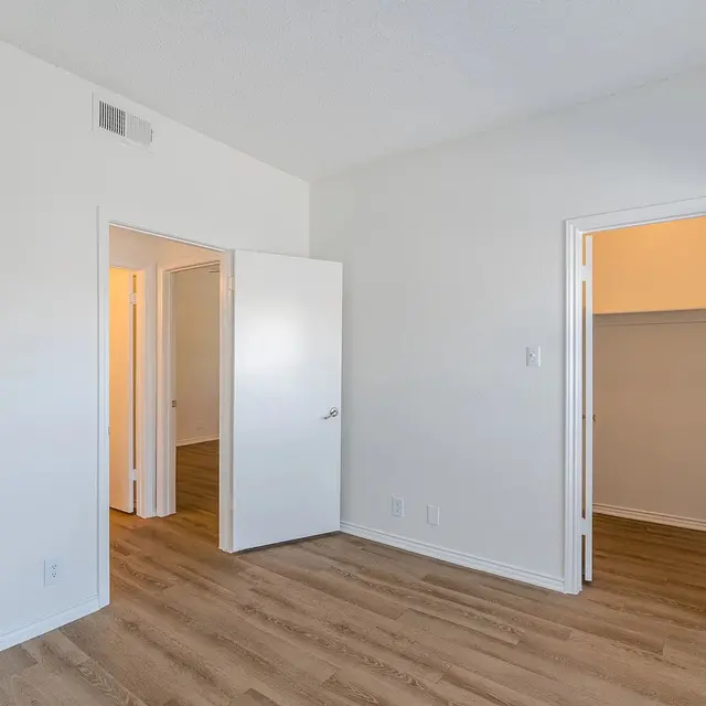 An empty room featuring light wooden flooring, white walls, and multiple doors leading to closets and adjacent spaces.