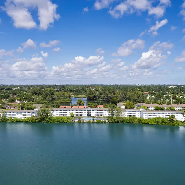 Aerial view showcasing a serene lake bordered by residential apartments under a bright blue sky with scattered clouds.