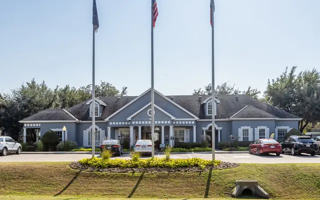A front view of a blue building with multiple flags in front, surrounded by greenery and cars parked on the driveway.