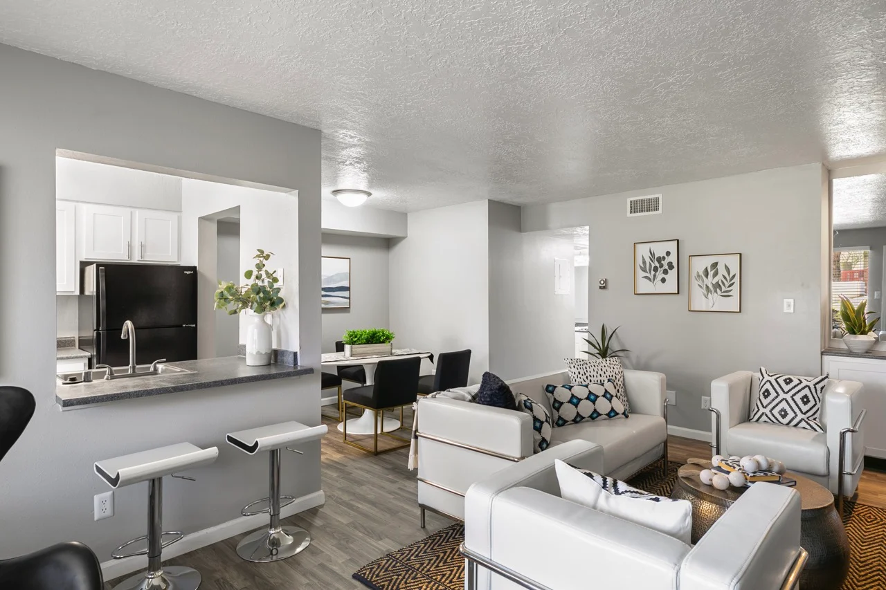 A modern living room with white sofas, a black bar area, and a kitchen visible in the background.