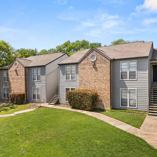 View of a two-story apartment complex surrounded by green grass and trees.