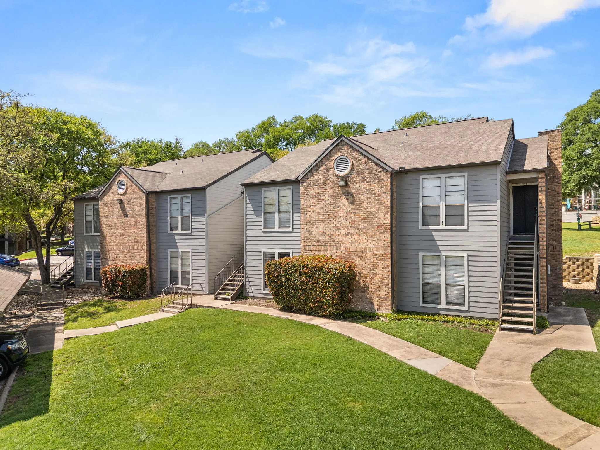 View of a two-story apartment complex surrounded by green grass and trees.