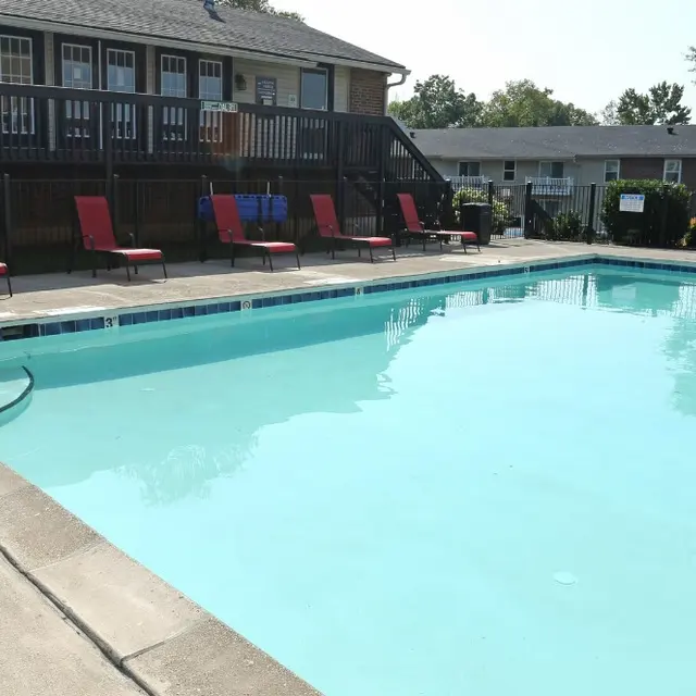A clear swimming pool with lounge chairs nearby, set in a residential area on a sunny day.