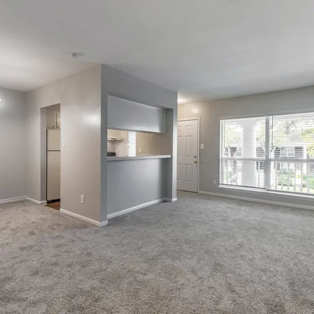 Spacious interior of a living room with gray carpet, neutral walls, and a large window.