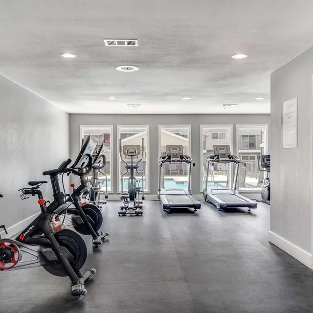 Fitness center at North Star Apartments with fitness equipment such as stationary bikes, treadmills, and ellipticals looking out at resident pool.