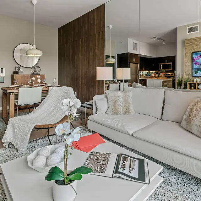 A living room with a couch, table, and a chair, situated next to a dining room table set for four.