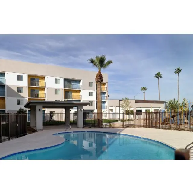 Apartment Complex with Swimming Pool A residential apartment complex with a swimming pool in the foreground. The building features multiple floors and balconies, surrounded by palm trees and a playground area.