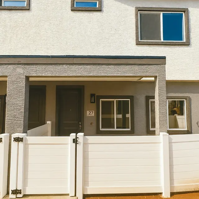 Modern Townhouse Exterior A modern townhouse exterior with a grey-white color scheme and a white fence. The entrance is visible, featuring a numbered door and several windows.