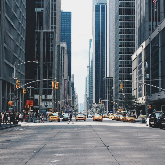 Busy city street with yellow taxis, skyscrapers, and pedestrians. Bright day with a clear sky and modern urban architecture.