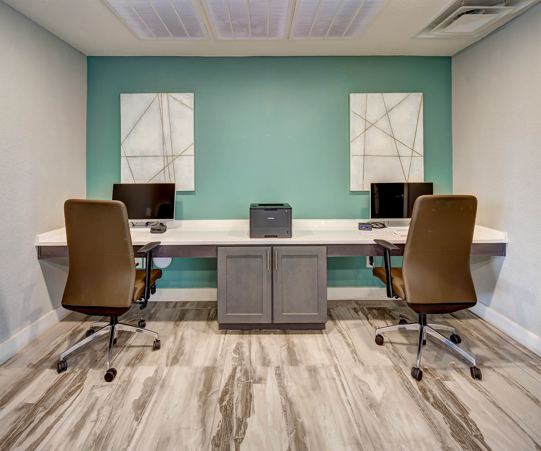 Community business center of our apartments, furnished with work desk, and chairs, desktop computer, a printer, and cabinets